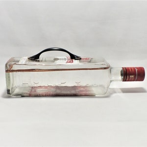 May include: A clear glass bottle with a black handle and a red cap. The bottle is empty and has a textured surface.