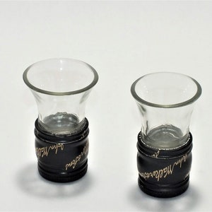 May include: Two clear glass shot glasses with black bases. The bases are wrapped with a black band with gold lettering that reads "Johnnie Walker" and "Red Label".
