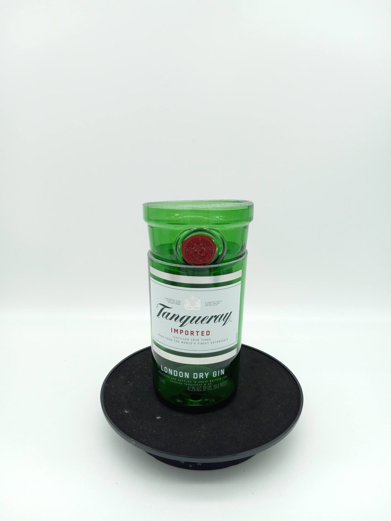 K&ouml;nnte beinhalten: Eine gr&uuml;ne Glasflasche Tanqueray London Dry Gin. Die Flasche steht auf einem schwarzen Drehteller. Das Etikett lautet "Tanqueray Importiert London Dry Gin."