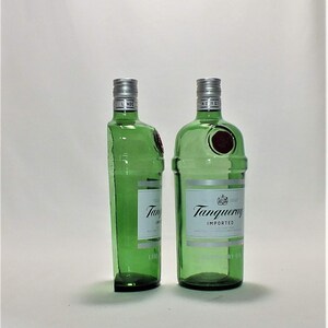 Op de afbeelding: Twee groene glazen flessen Tanqueray Imported Gin. De flessen staan rechtop op een wit oppervlak.