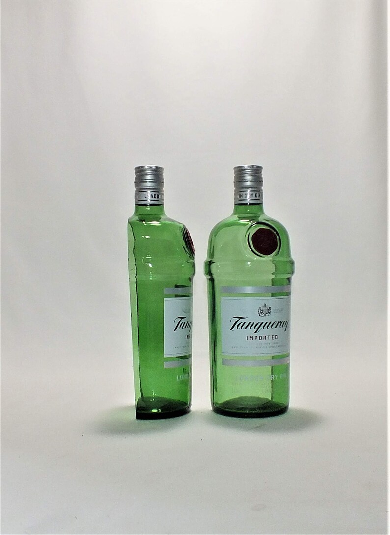 Op de afbeelding: Twee groene glazen flessen Tanqueray Imported Gin. De flessen staan rechtop op een wit oppervlak.