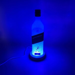 Pode incluir: Uma luz LED azul em forma de garrafa de whisky Johnnie Walker de 12 anos. A garrafa &eacute; fosca e o r&oacute;tulo &eacute; vis&iacute;vel.