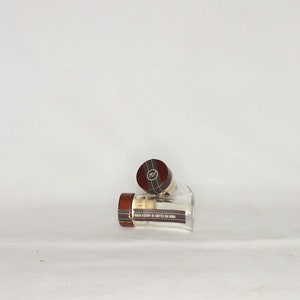 May include: Two clear glass bottles with brown wooden lids. The lids have a gold label with black text.