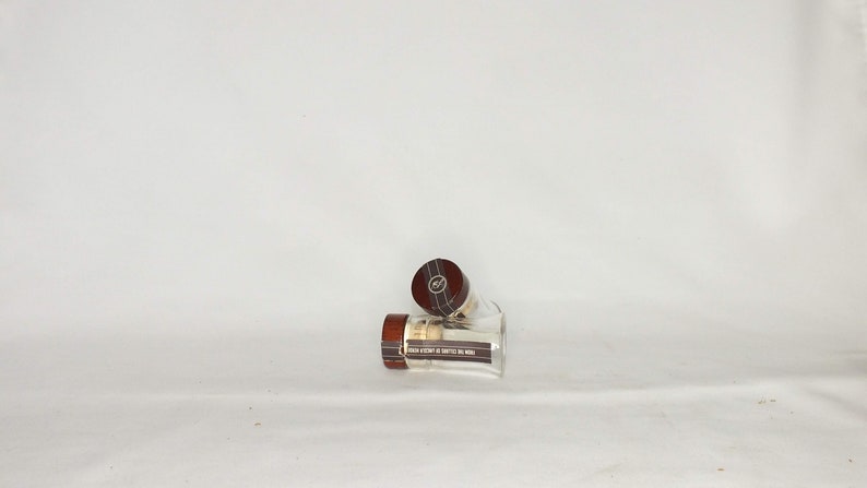 May include: Two clear glass bottles with brown wooden lids. The lids have a gold label with black text.
