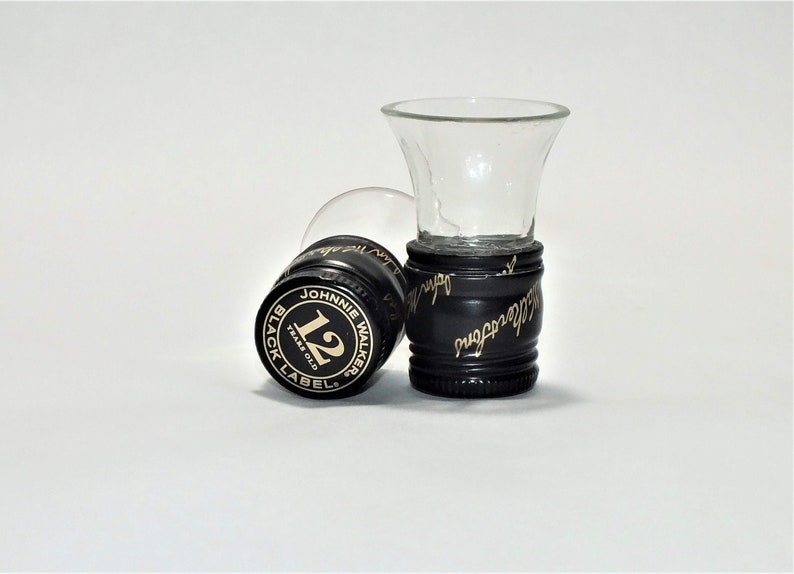 May include: Two black and gold Johnnie Walker Black Label 12 year old Scotch Whisky bottle caps used as shot glasses.