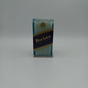 May include: A blue glass candle with a white wax top. The candle has a label that reads "Johnnie Walker Blue Label Blended Scotch Whisky" and a gold crest.