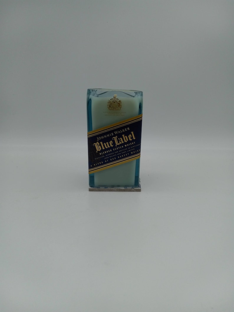 May include: A blue glass candle with a white wax top. The candle has a label that reads "Johnnie Walker Blue Label Blended Scotch Whisky" and a gold crest.