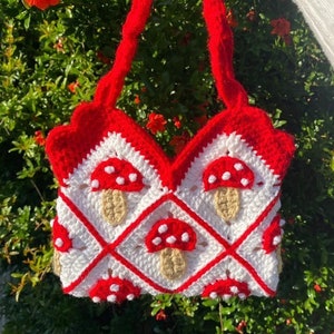 Puede incluir: Un bolso de crochet con un patrón rojo y blanco con setas. El bolso tiene una parte superior festoneada y dos asas.