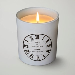 Puede incluir: Vela blanca con un diseño de esfera de reloj que dice "TIME to RECONCILE MUSK www.evelyn48.com". La vela está encendida y la llama es visible.