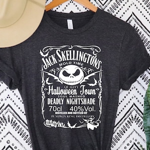 May include: Dark gray t-shirt with a white graphic featuring Jack Skellington from The Nightmare Before Christmas. The graphic includes text that reads "Jack Skellington's Mold Time Halloween Town Deadly Nightshade 70cl 40%Vol."