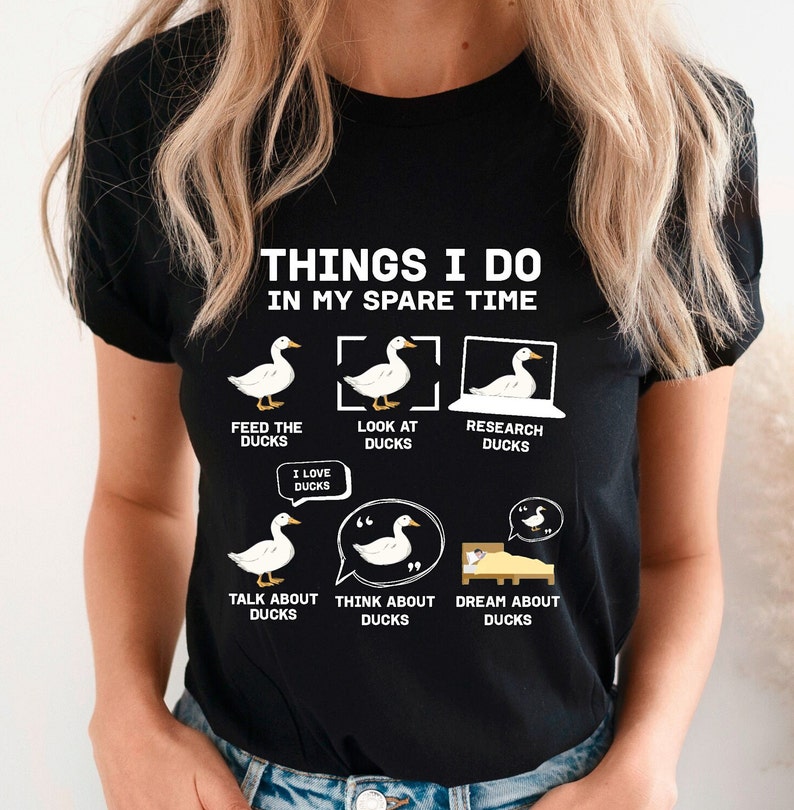 K&ouml;nnte beinhalten: Schwarzes T-Shirt mit dem Text "THINGS I DO IN MY SPARE TIME" und Enten-Illustrationen. Das Design zeigt Aktivit&auml;ten wie F&uuml;ttern, Betrachten und Recherchieren von Enten sowie "I LOVE DUCKS".