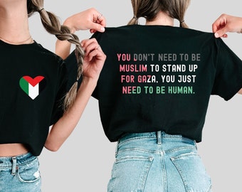 May include: Black t-shirt featuring a heart-shaped Palestinian flag on the front. The back of the shirt has the text: "YOU DON'T NEED TO BE MUSLIM TO STAND UP FOR GAZA, YOU JUST NEED TO BE HUMAN." The text is in pink, green, and white.