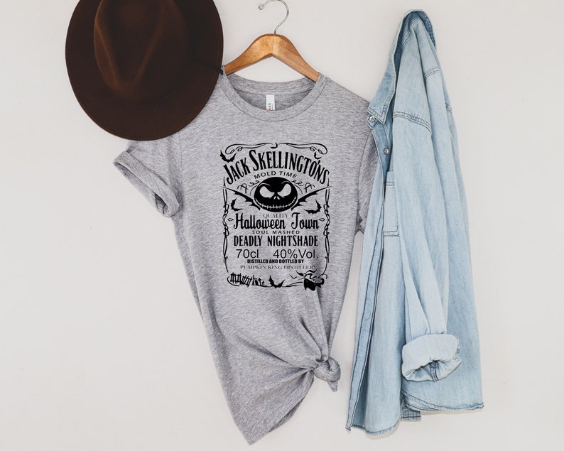 May include: A gray t-shirt with a black graphic design featuring the text "Jack Skellington's Mold Time" and "Halloween Town." The design includes a Jack Skellington face and the words "Deadly Nightshade" and "70cl 40%Vol."