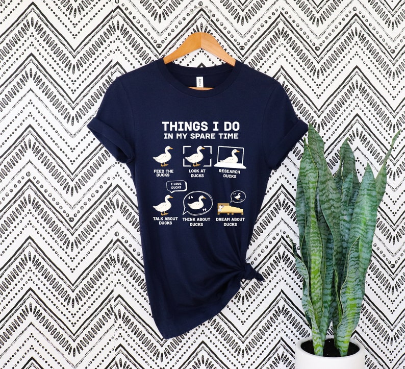 K&ouml;nnte beinhalten: Marineblaues T-Shirt mit dem Text "THINGS I DO IN MY SPARE TIME" und Enten-Illustrationen. Das Design zeigt Enten bei verschiedenen Aktivit&auml;ten, wie F&uuml;ttern, Betrachten und Erforschen von Enten.