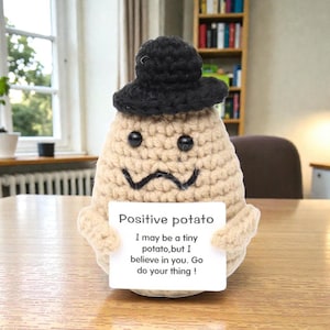 May include: A crocheted potato figure with a black hat and a mustache. The potato holds a sign that reads "Positive potato. I may be a tiny potato, but I believe in you. Go do your thing!"