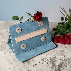 May include: A light blue leather-like tablet case with a wooden ruler and heart-shaped magnets. A red rose is placed on top of the case. The ruler measures up to 20 cm, or approximately 8 inches.