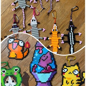 May include: A collection of colorful plastic bead art keychains featuring various animal and character designs, including possums, a lizard, a frog-hooded cat, a lava lamp, and cartoon creatures, each attached to a metal carabiner clip.