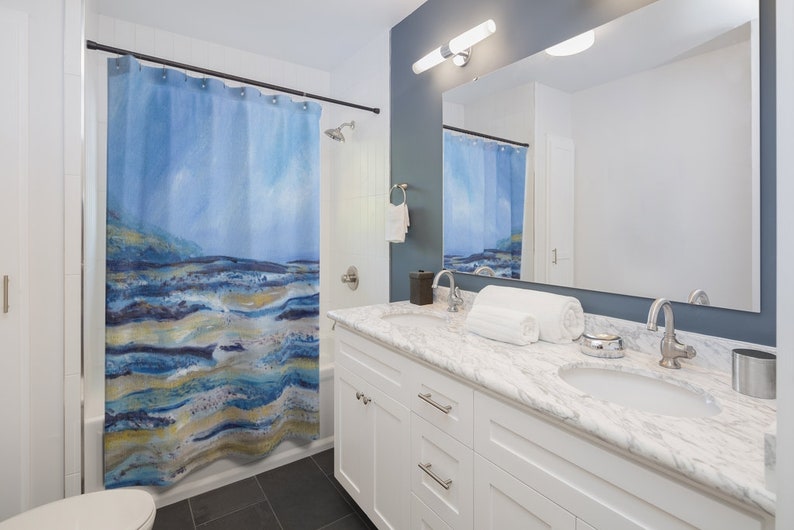 May include: A blue and white abstract art shower curtain with a landscape design. The curtain hangs in a bathroom with a white vanity, marble countertop, and a large mirror. The shower curtain has a watercolor effect.