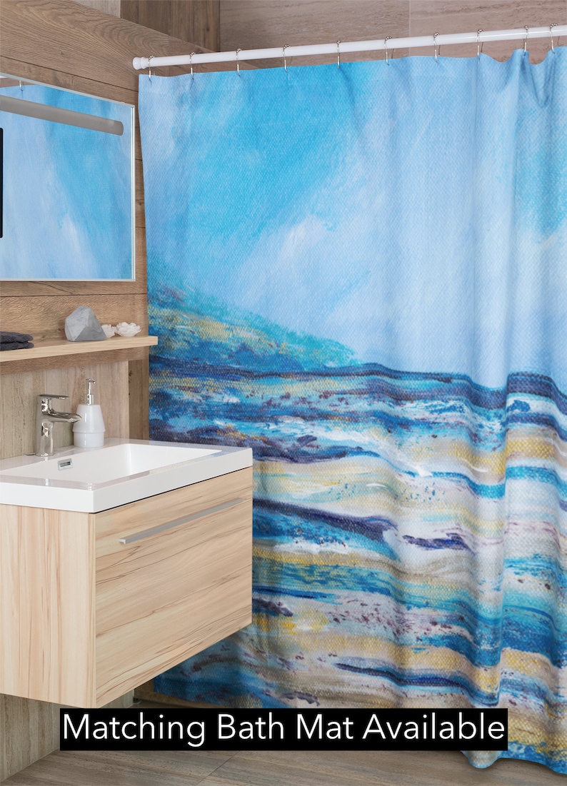 May include: A blue and white abstract art shower curtain with a coastal theme. The curtain features a painted design with shades of blue, white, and gold, evoking a beach or ocean scene. Text at the bottom reads "Matching Bath Mat Available."