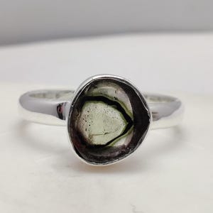 May include: A silver ring with a green and black gemstone set in a bezel setting.