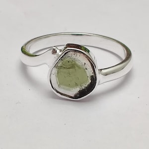 以下が含まれることがあります： 緑色の宝石がベゼル留めされたシルバーリング。リングはシンプルで湾曲したバンドです。