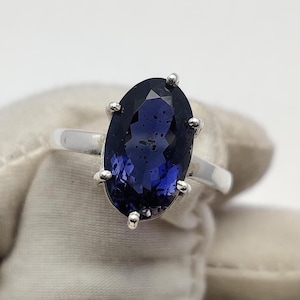 May include: A silver ring featuring a large, oval-cut, deep blue gemstone. The gemstone is held in place by six silver prongs. The ring's band is a simple, polished silver.