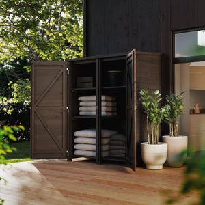 May include: A dark brown wooden storage cabinet with two doors open, revealing shelves with folded white towels and other items. The cabinet is on a wooden deck, with potted plants nearby. The doors have a diagonal cross design.
