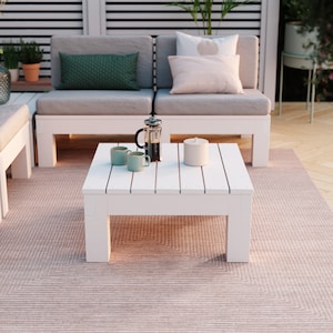 Può includere: Un tavolino quadrato in legno bianco con superficie a doghe. Sul tavolo sono appoggiate due tazze verde chiaro, una caffettiera a stantuffo in vetro con manico nero e un contenitore cilindrico bianco semplice con coperchio.