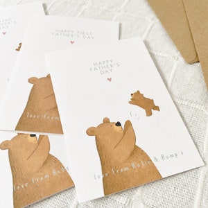 May include: A set of four cards with a brown bear illustration. The cards say "Happy First Father's Day" and "Happy Father's Day". The cards are personalized with the text "love from Baby" and "love from Katie & Bump x".