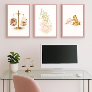 May include: Three framed art prints with pink borders. The prints depict legal themes: a scale of justice, Lady Justice, and a gavel, each adorned with floral accents. The artwork is displayed above a desk with a computer and a small decorative scale.