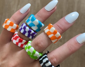 May include: A set of seven checkerboard patterned rings in various colours, including orange, red, green, purple, blue, black and white. The rings are stacked on a hand.
