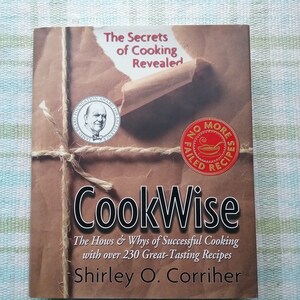 May include: A brown cookbook with a title that reads "CookWise: The Hows & Whys of Successful Cooking with over 230 Great-Tasting Recipes" by Shirley O. Corriher. The cover features a brown paper package with twine and two red seals.