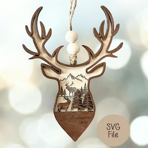 May include: Wooden deer head ornament with a mountain and forest scene. The ornament has a brown outline and a light wood interior. The bottom of the ornament has the text "The Anderson Family". Two wooden beads and a twine loop are at the top.