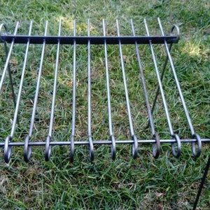Puede incluir: Un soporte de parrilla de metal con múltiples pinchos, ideal para cocinar brochetas o pinchos sobre fuego abierto. El soporte está hecho de metal resistente y tiene un diseño simple.