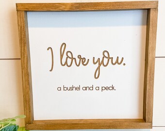 May include: A wooden framed sign with the text "I love you. A bushel and a peck." in brown lettering on a white background.