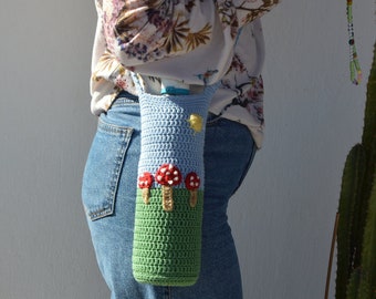 May include: A crocheted blue and green bottle holder with red and yellow mushroom accents. The holder is worn as a crossbody bag.