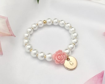 May include: A white pearl bracelet with a pink flower charm and a gold initial charm. The initial charm is a letter C.