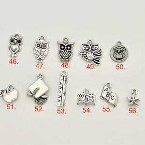 May include: A set of 12 silver charm pendants with various school-themed designs, including owls, a graduation cap, a ruler, a book, an apple, and a star. The charms are numbered 46 through 56.