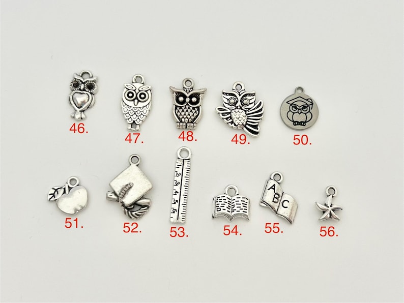 May include: A set of 12 silver charm pendants with various school-themed designs, including owls, a graduation cap, a ruler, a book, an apple, and a star. The charms are numbered 46 through 56.