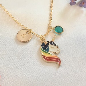 May include: Gold necklace with a unicorn charm, a small round charm with the letter A, and a teal blue gemstone. The unicorn charm has a rainbow mane and tail.