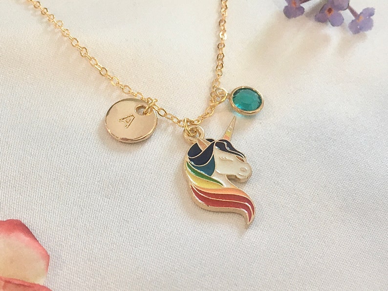 May include: Gold necklace with a unicorn charm, a small round charm with the letter A, and a teal blue gemstone. The unicorn charm has a rainbow mane and tail.