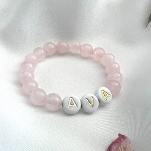 May include: A pink gemstone bracelet with white beads that spell out the name "AVA".