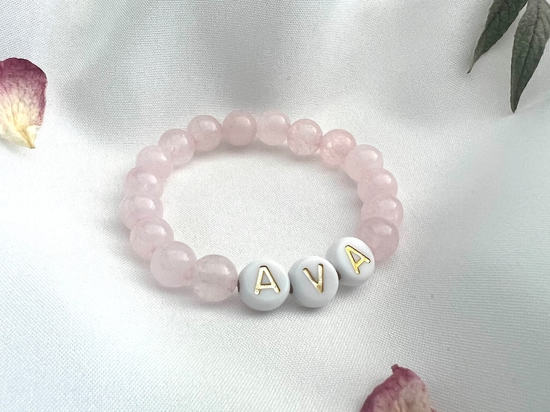 May include: A pink gemstone bracelet with white beads that spell out the name "AVA".