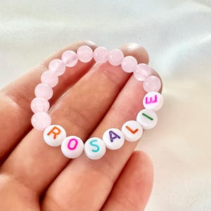 May include: A pink and white beaded bracelet with the name "ROSALIE" spelled out in colorful letters.