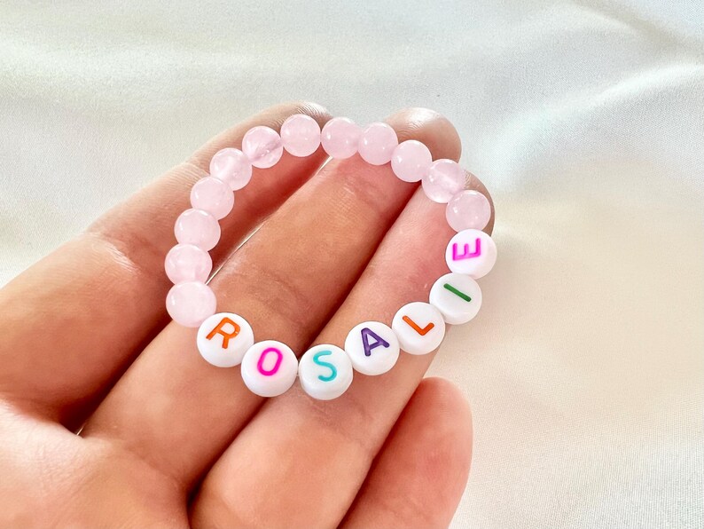 May include: A pink and white beaded bracelet with the name "ROSALIE" spelled out in colorful letters.
