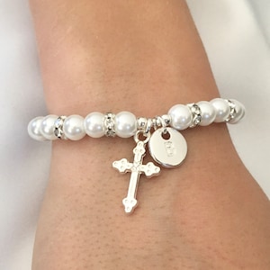 May include: A white pearl bracelet with a silver cross and a silver charm with the letter "B" on it.