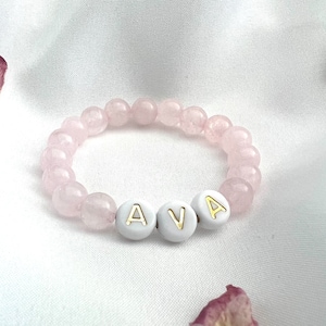 May include: A pink beaded bracelet with white beads that spell out the name "AVA".