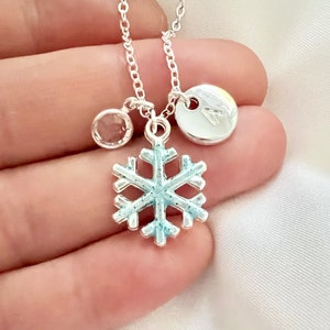 May include: Silver necklace with a snowflake charm, a clear crystal charm, and a silver disc charm with the letter A.