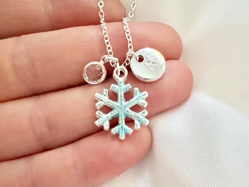 May include: Silver necklace with a snowflake charm, a clear crystal charm, and a silver disc charm with the letter A.