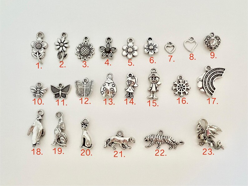 May include: Twenty-three silver charm pendants with various designs, including flowers, animals, and abstract shapes. The charms are numbered 1 through 23.